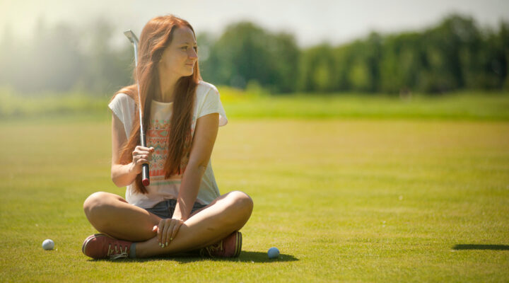 Canva Woman in White Scoop neck Shirt and Blue Shorts Holding a Golf Club Sitting on Golf Field